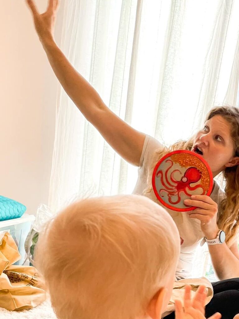 Nauczycielka pokazuje dzieciom krążek sensoryczny z ośmiornicą, z ręką wzniesioną do góry